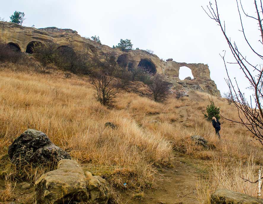 арочные формы горы и тропа с поднимающимся наверх по склону туристом